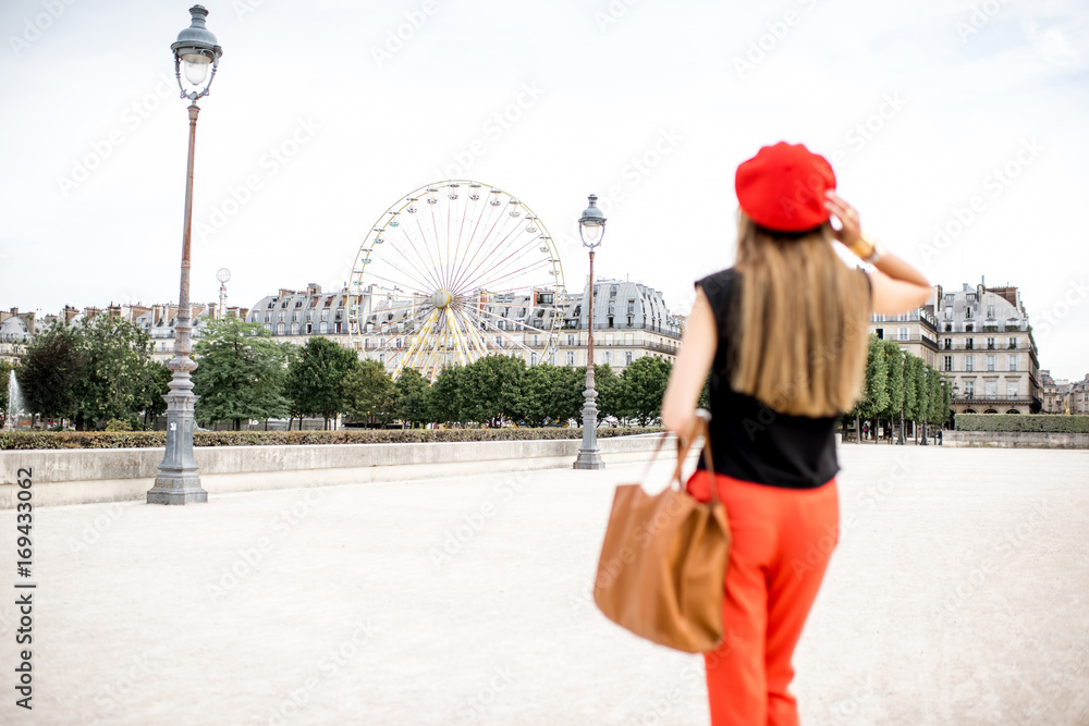 戴着红帽子、穿着红裤子的年轻女子在巴黎杜乐丽公园散步，背景是摆轮