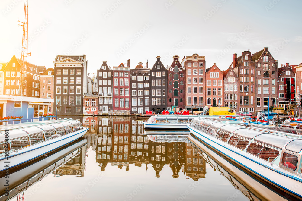 Morning view on the beautiful buildings and boats on the Damrak avenue in Amsterdam