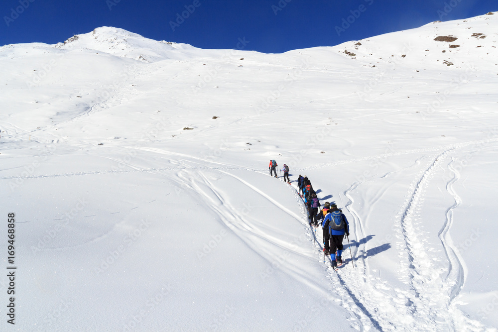 Group of people hiking on snowshoes and mountain snow panorama with blue sky in Stubai Alps, Austria