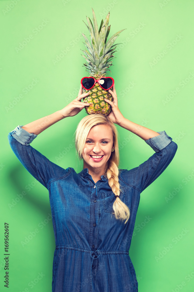  Happy young woman holding a pineapple on a green background