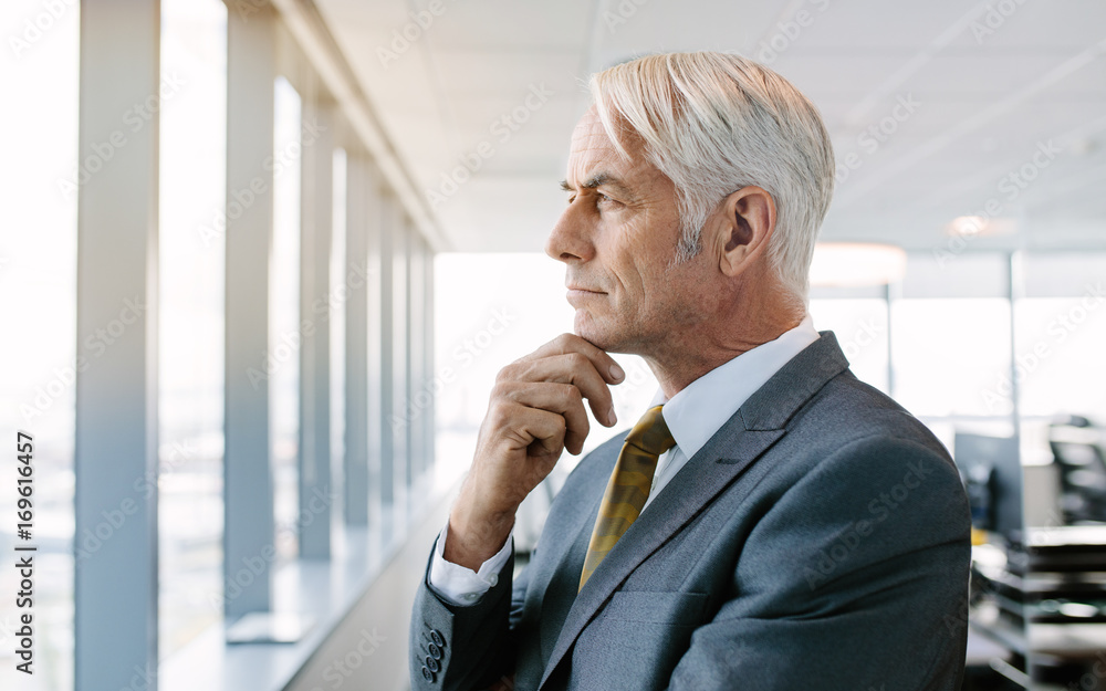 Thoughtful senior businessman standing by window