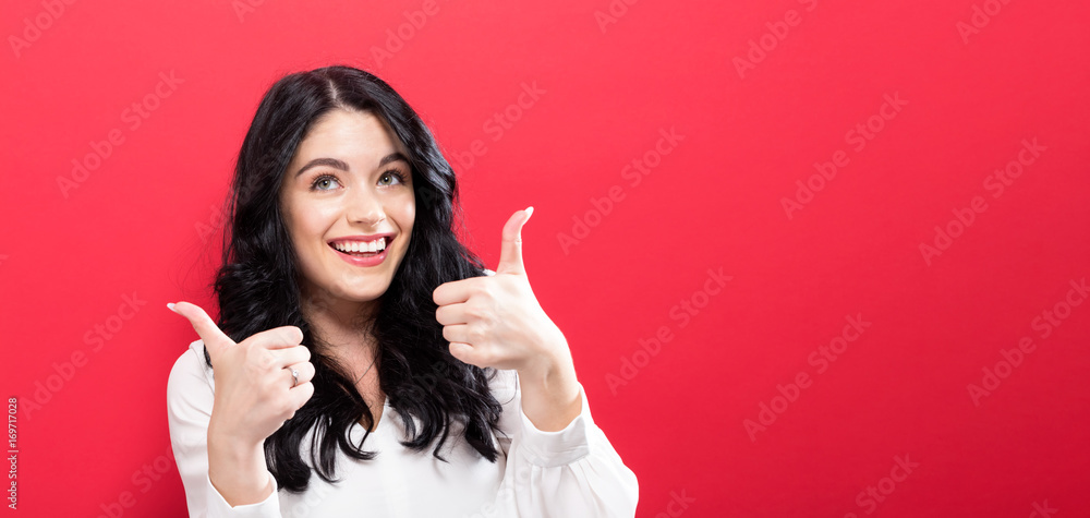 Happy young woman giving thumbs up on a solid background