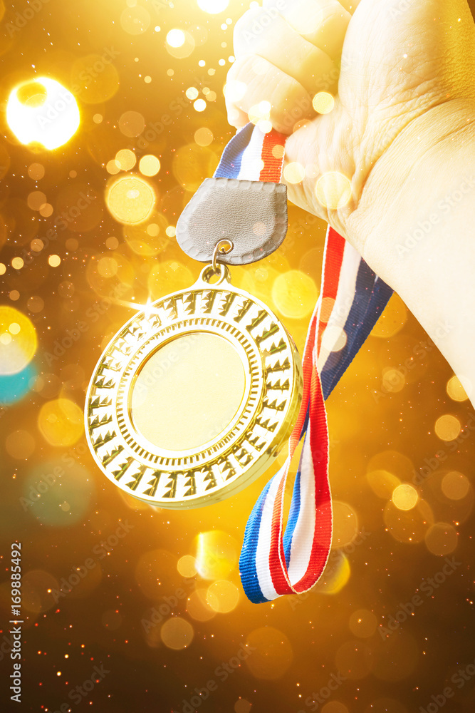 Hand raised, holding gold medal with abstract shiny lights . award and victory concept .