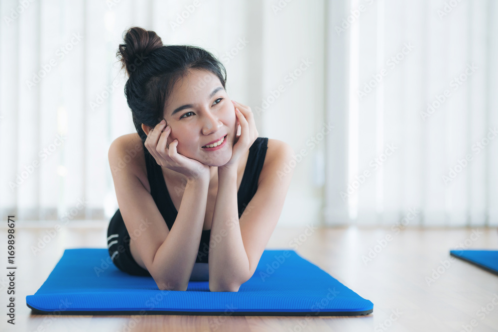 Young happy woman relaxing on yoga mat in gym