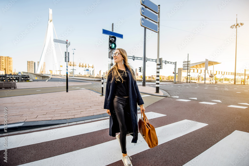 Stylish businesswoman crossing the street at the modern district during the morning in Rotterdam cit