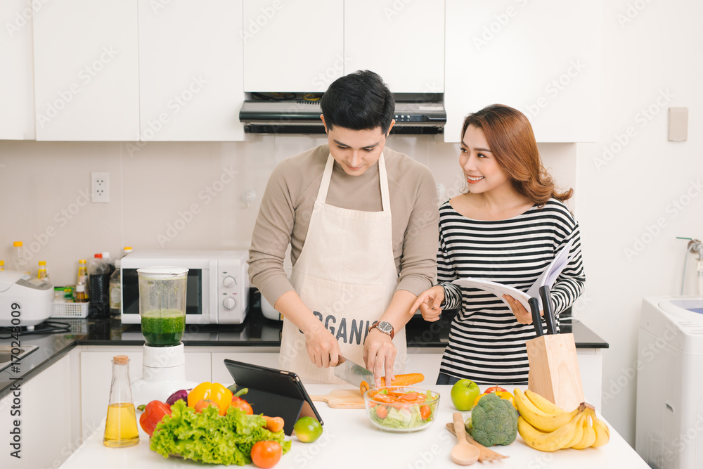 幸福的一对夫妻在厨房里。一个男人在切蔬菜和做沙拉，而他的妻子在读rec