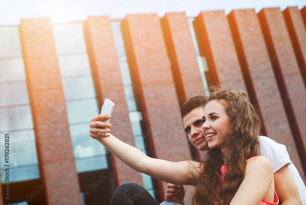 Young couple sitting in town outdoor with mobile phone taking selfie