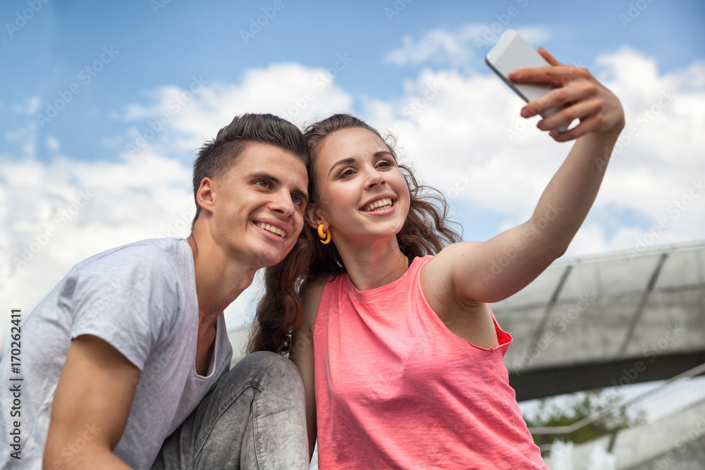 Young couple sitting in town outdoor with mobile phone taking selfie