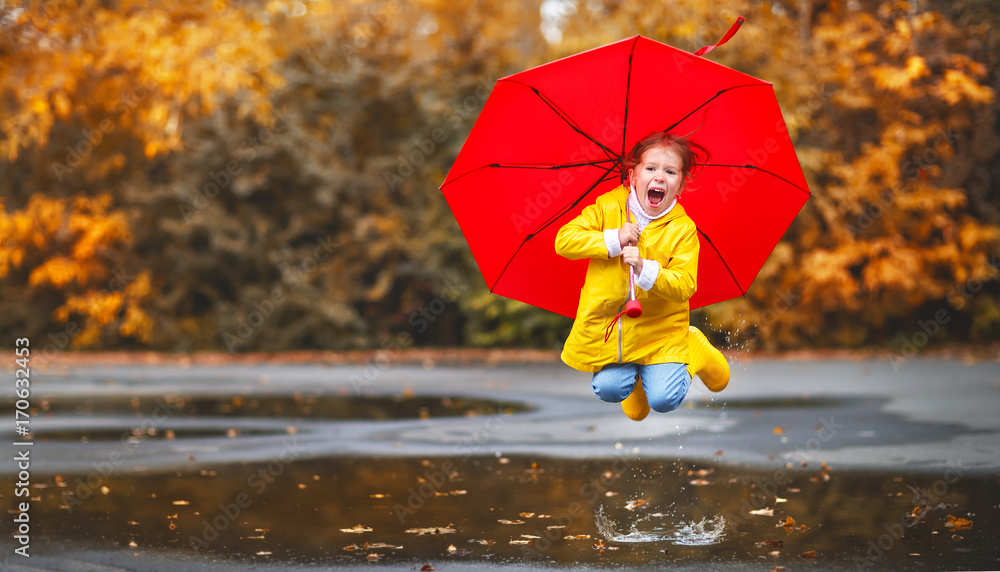 快乐的小女孩，带着雨伞和橡胶靴在水坑里秋天散步