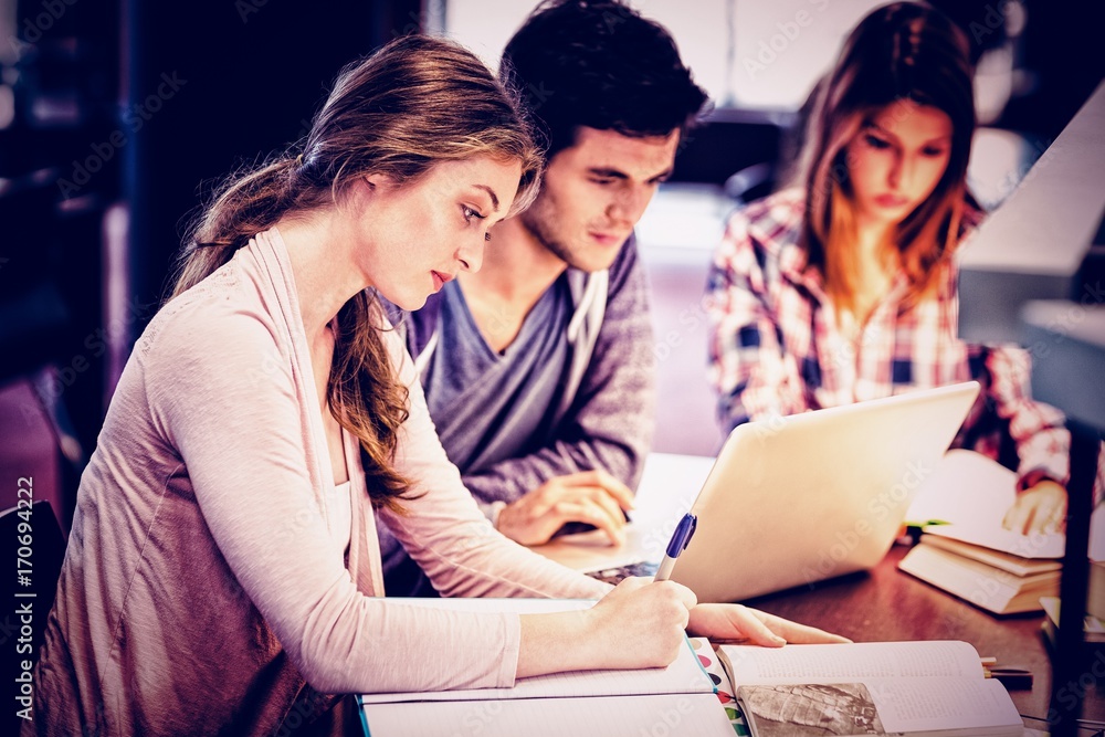 Focused classmates studying together while using laptop