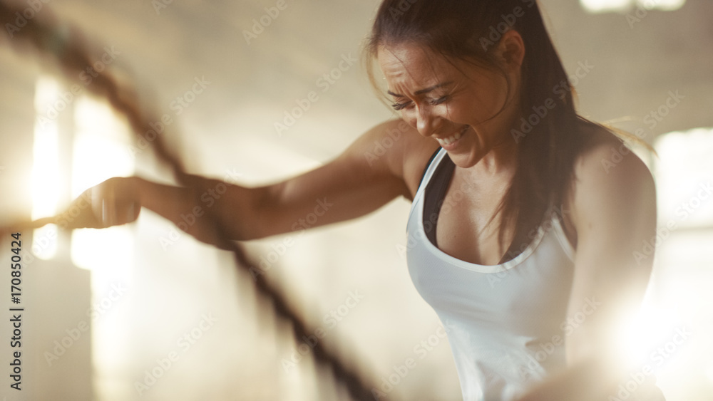 Athletic Female in a Gym Exercises with Battle Ropes During Her Cross Fitness Workout/ High-Intensit