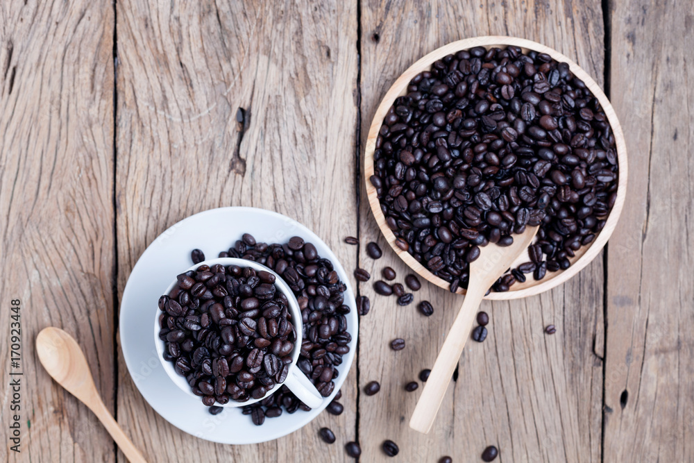 wooden spoon with coffee beans in coffee cup on old wooden plank background.