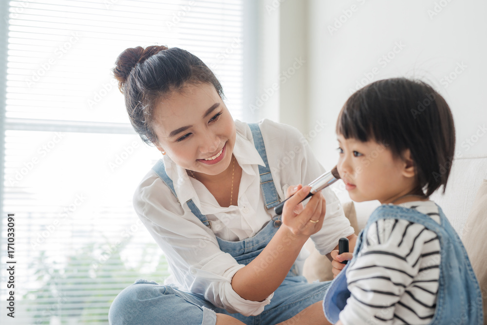 可爱的小女孩和她美丽的母亲坐在家里的沙发上化妆