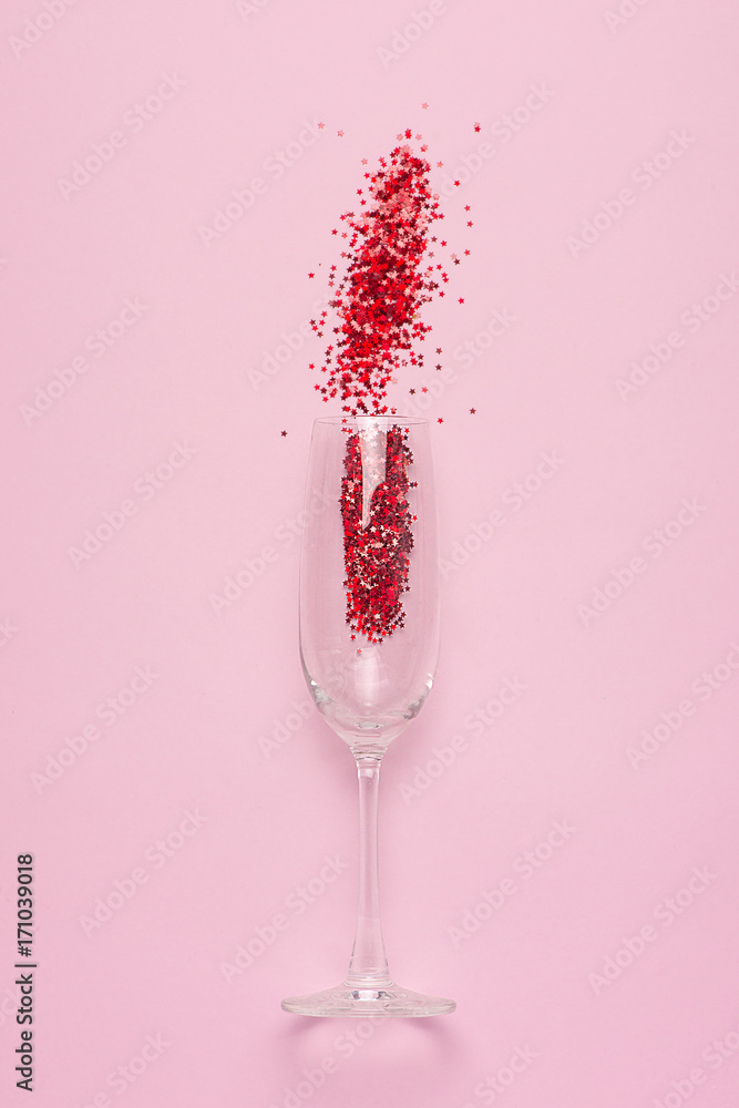 Flat lay of Celebration. Champagne glass with colorful party streamers on pink background.