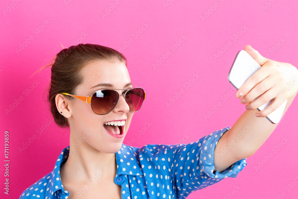 Young woman taking a selfie on a pink background