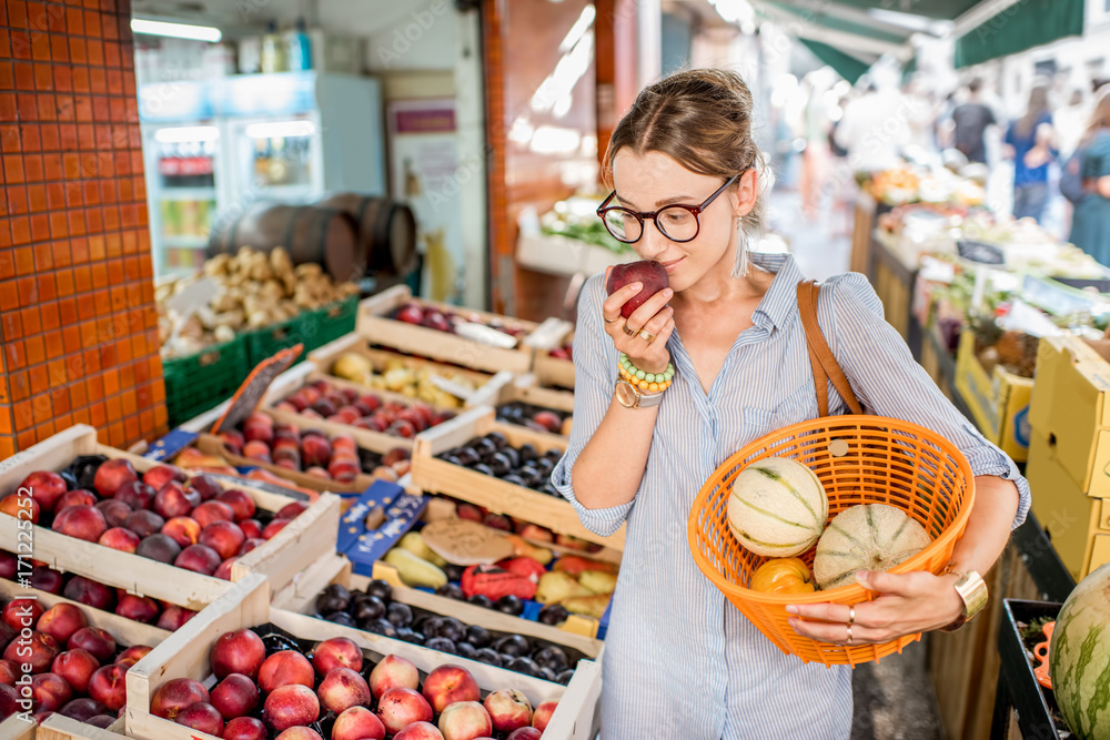 Young woman choosing a fresh peach standing with basket at the food market in France