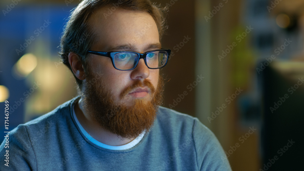 Young Bearded Creative Man With Glasses Thinks on a Problem While Working on His Personal Computer.