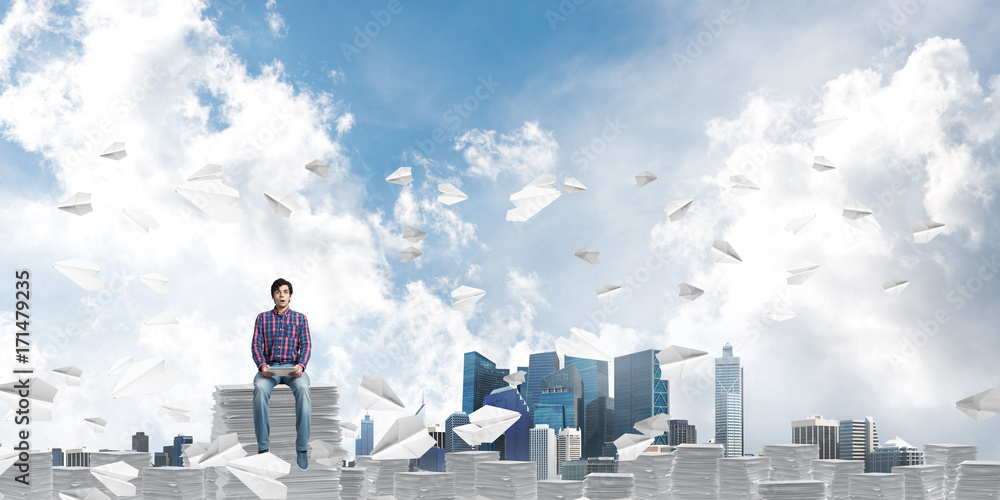 Attractive man sitting on pile of paper documents.