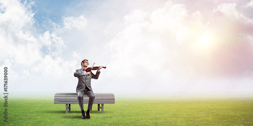 Handsome businessman in park on wooden bench play his melody