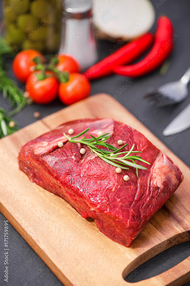 Raw beef on a cutting board  with spices and ingredients for cooking.