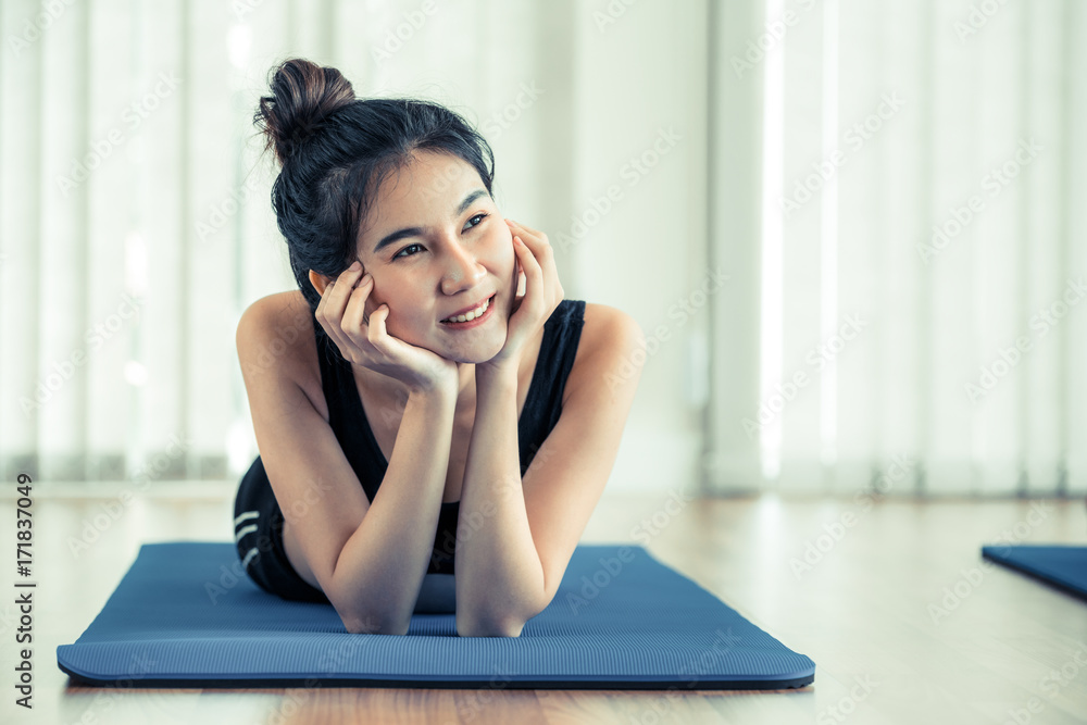 Young happy woman relaxing on yoga mat in gym