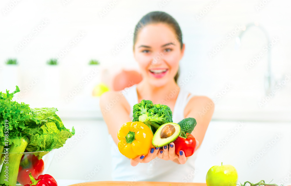 美丽的年轻女人在家里的厨房里拿着新鲜的蔬菜和水果。健康饮食理念