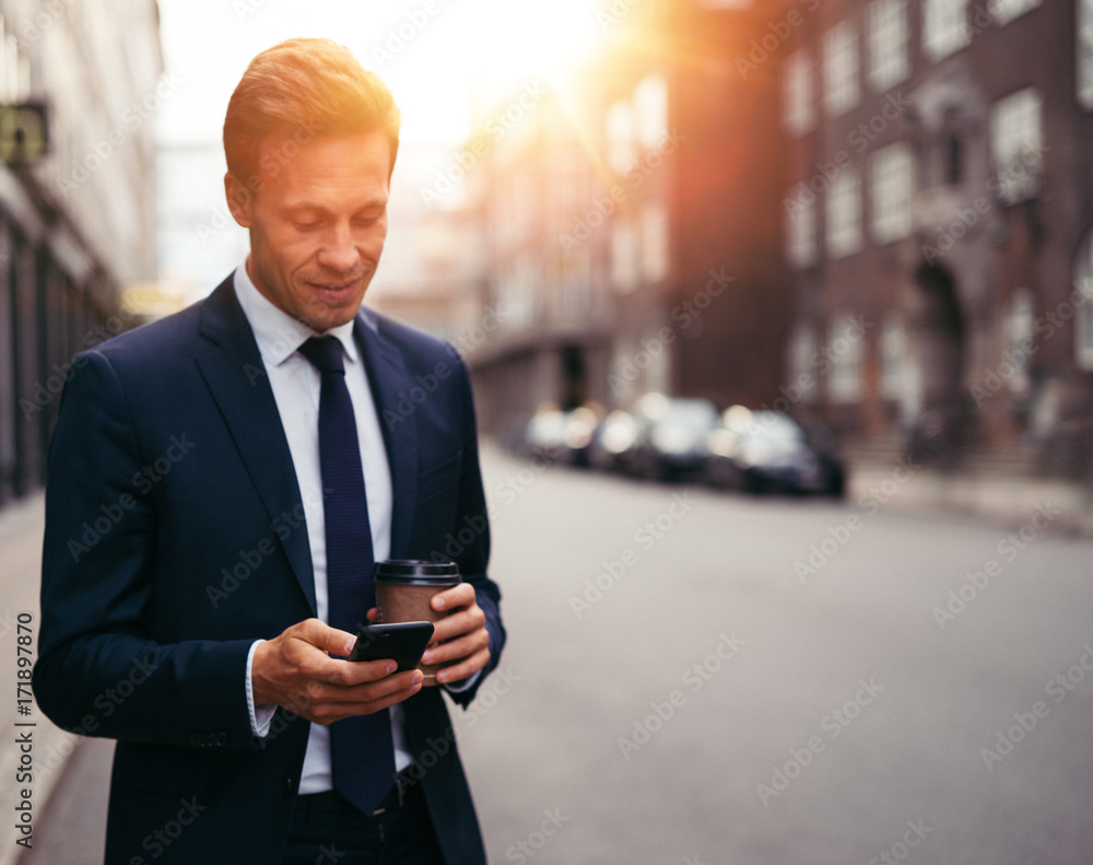 Businessman drinking coffee and reading messages on a city stree