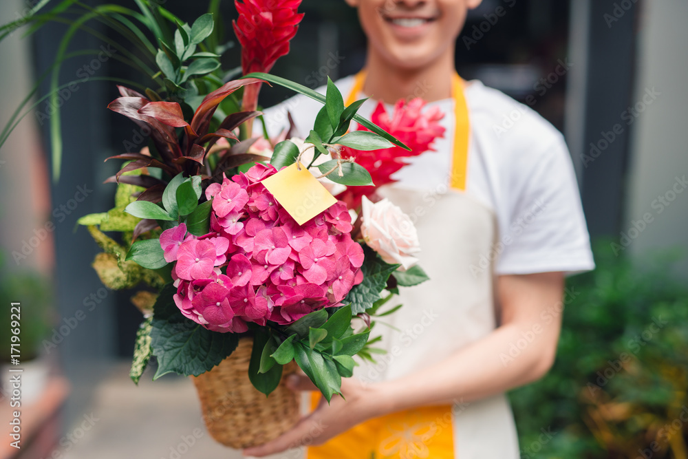 英俊的男花商站在花店里，手里拿着一束花