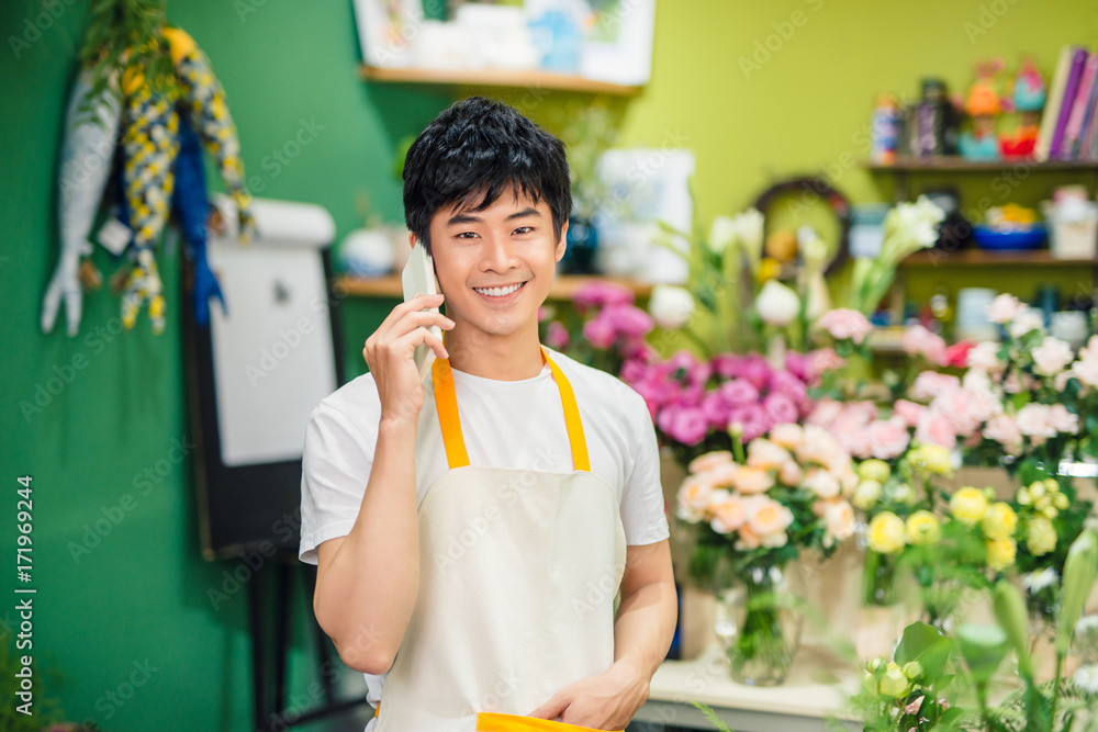 微笑的亚洲男性花商在花店用智能手机打电话。