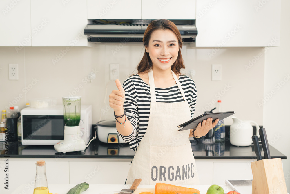 漂亮的年轻家庭主妇，在厨房里用平板电脑做饭