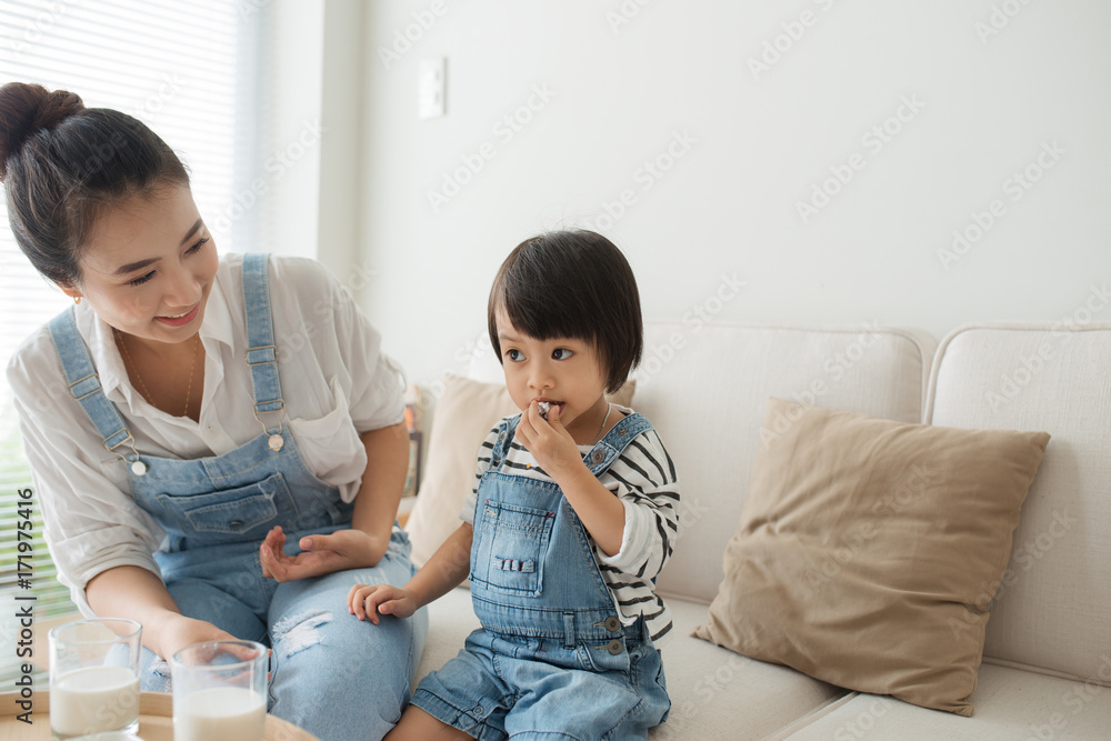 可爱的小女孩和她美丽的母亲喝牛奶吃饼干