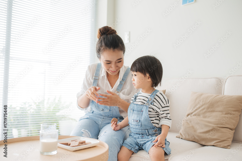 美丽的女人和她可爱的小女儿一边品尝饼干和牛奶一边微笑