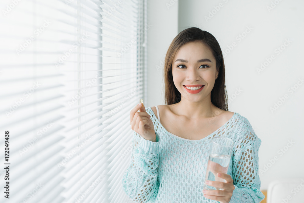 一位年轻的亚洲女性正在服用一片药丸和一杯水。