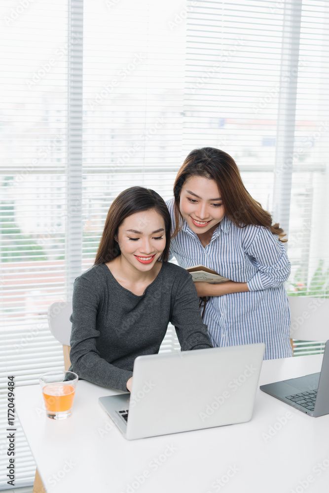 两位面带微笑的亚洲女商人在办公室里拿着笔记本电脑工作