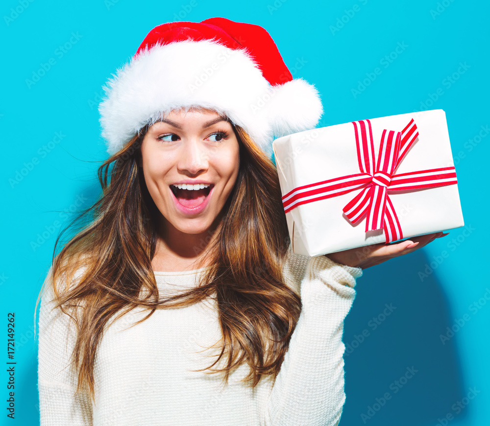 Happy young woman with Santa hat holding a Christmas present