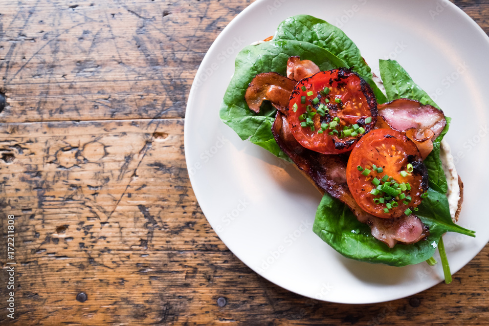 Plate with BLT toast with grilled tomatoes, bacon, lettuce and special sauce on the old wooden table