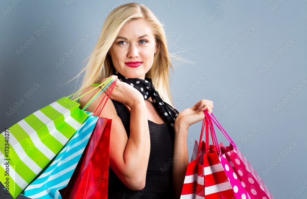 Happy young blonde woman with shopping bags on a gray background