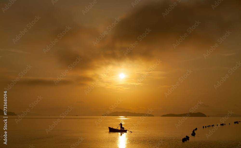 Fisherman with a paddle in small boat at the tropical sea with beautiful sunrise or sunset in phuket