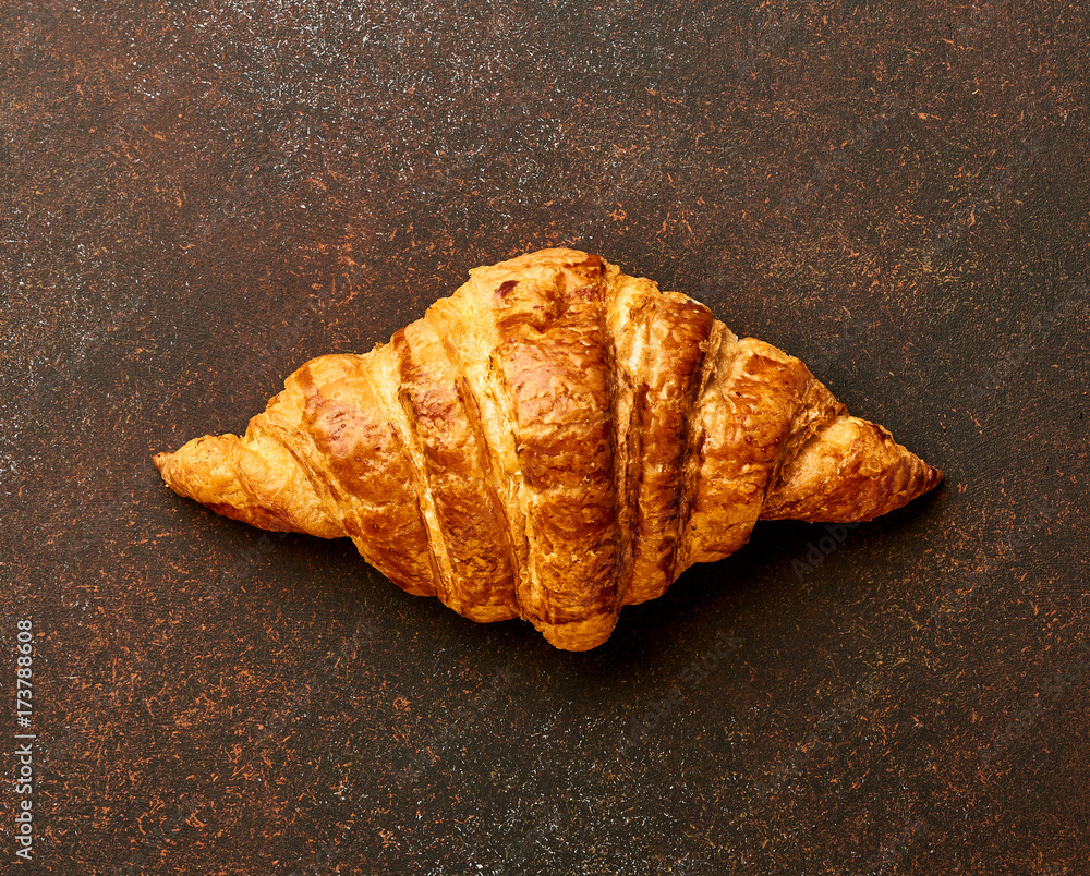 Croissant on brown concrete background. Bakery product. Top view.