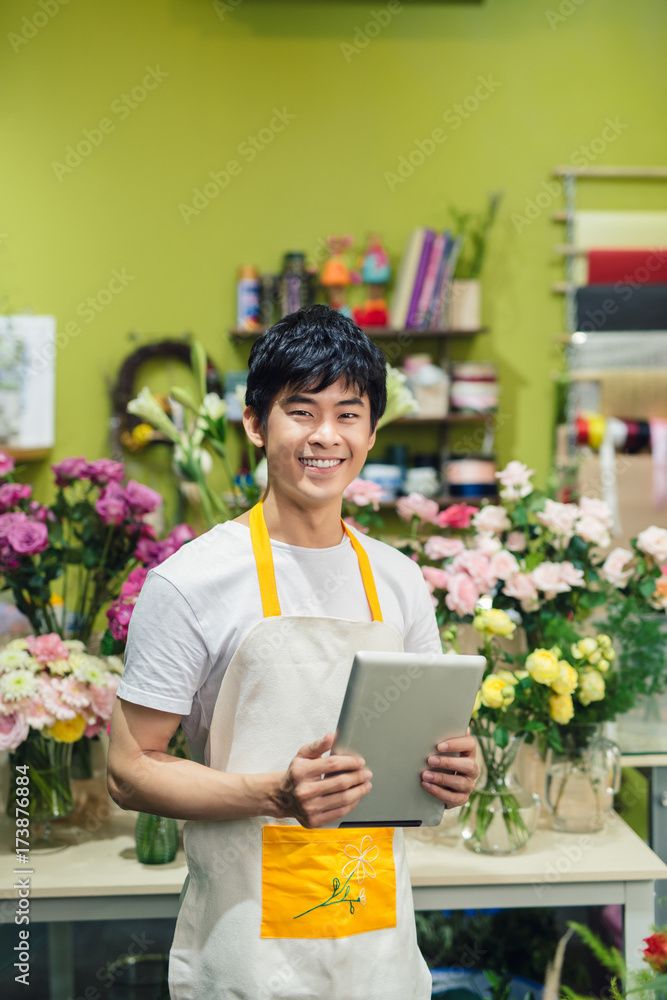 快乐的亚洲男性花商在花店柜台使用数字平板电脑