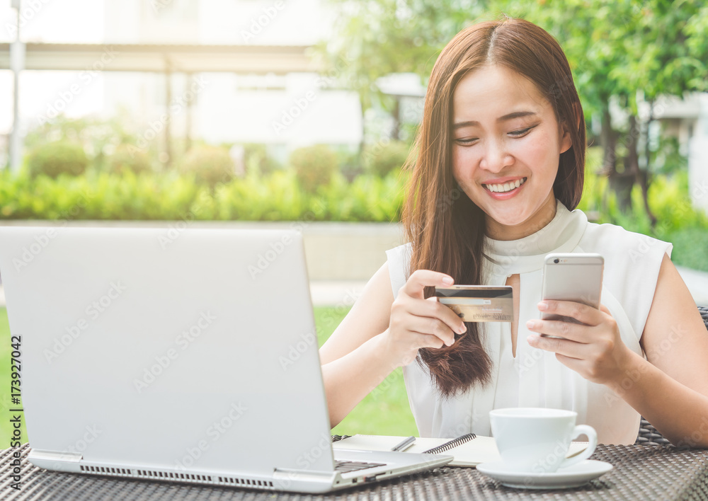 Young beautiful Asian woman using credit card and laptop for online shopping at outdoor park, smile/