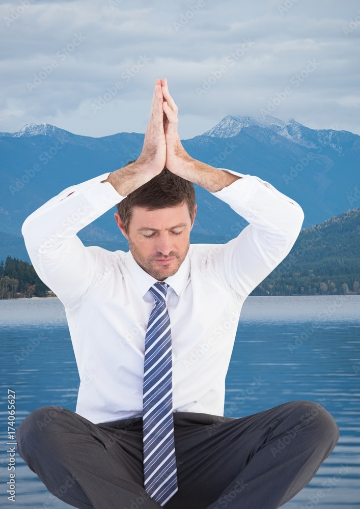 Business man meditating against water and mountains