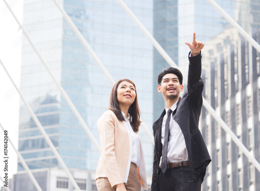 两位20-30岁的年轻亚洲商人女商人站在现代城市里，指出炫耀