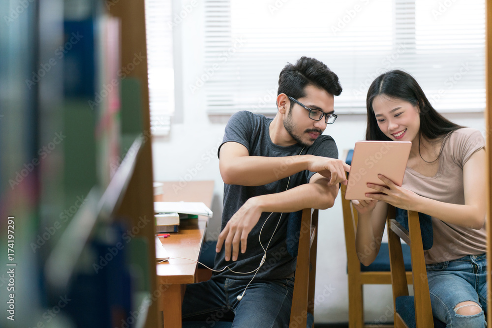 亚洲学生在平板电脑上互相帮助学习图书馆里的知识