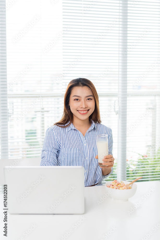 年轻迷人的亚洲女商人坐在办公桌前喝牛奶