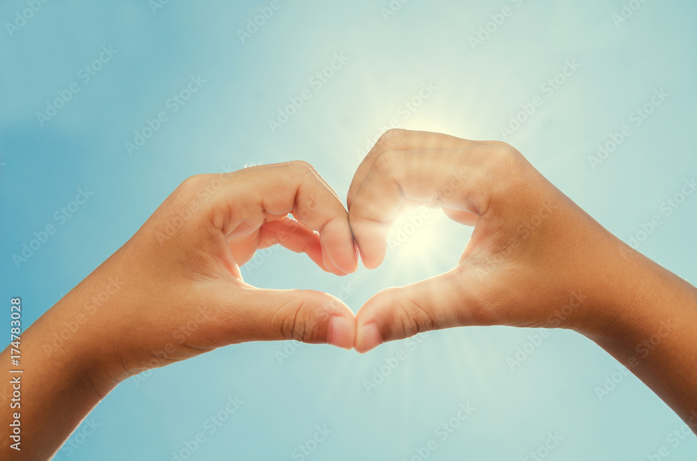 woman forming heart shaped hands with sun and blue sky background