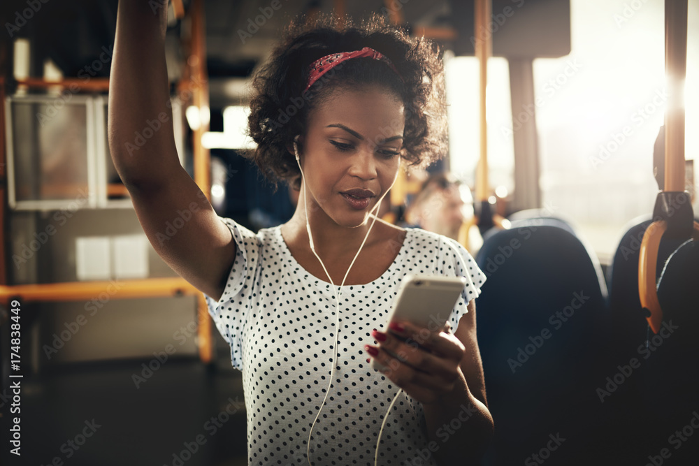 Young African woman standing on a bus listening to music