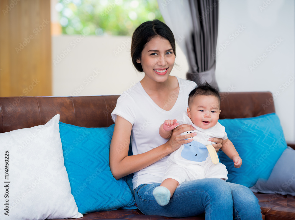 Mom and newborn baby sit and play togather on sofa