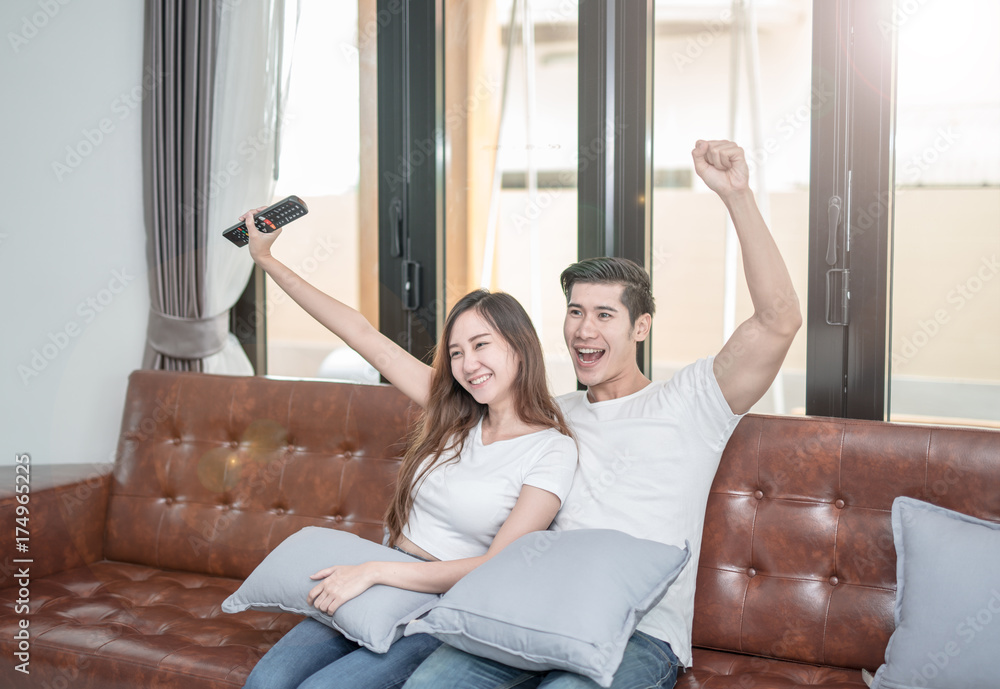 Asian couple watching TV sitting on a couch at home cheerful