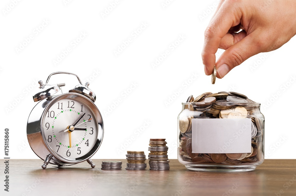 Hand putting coins in glass jar with retro alarm clock.